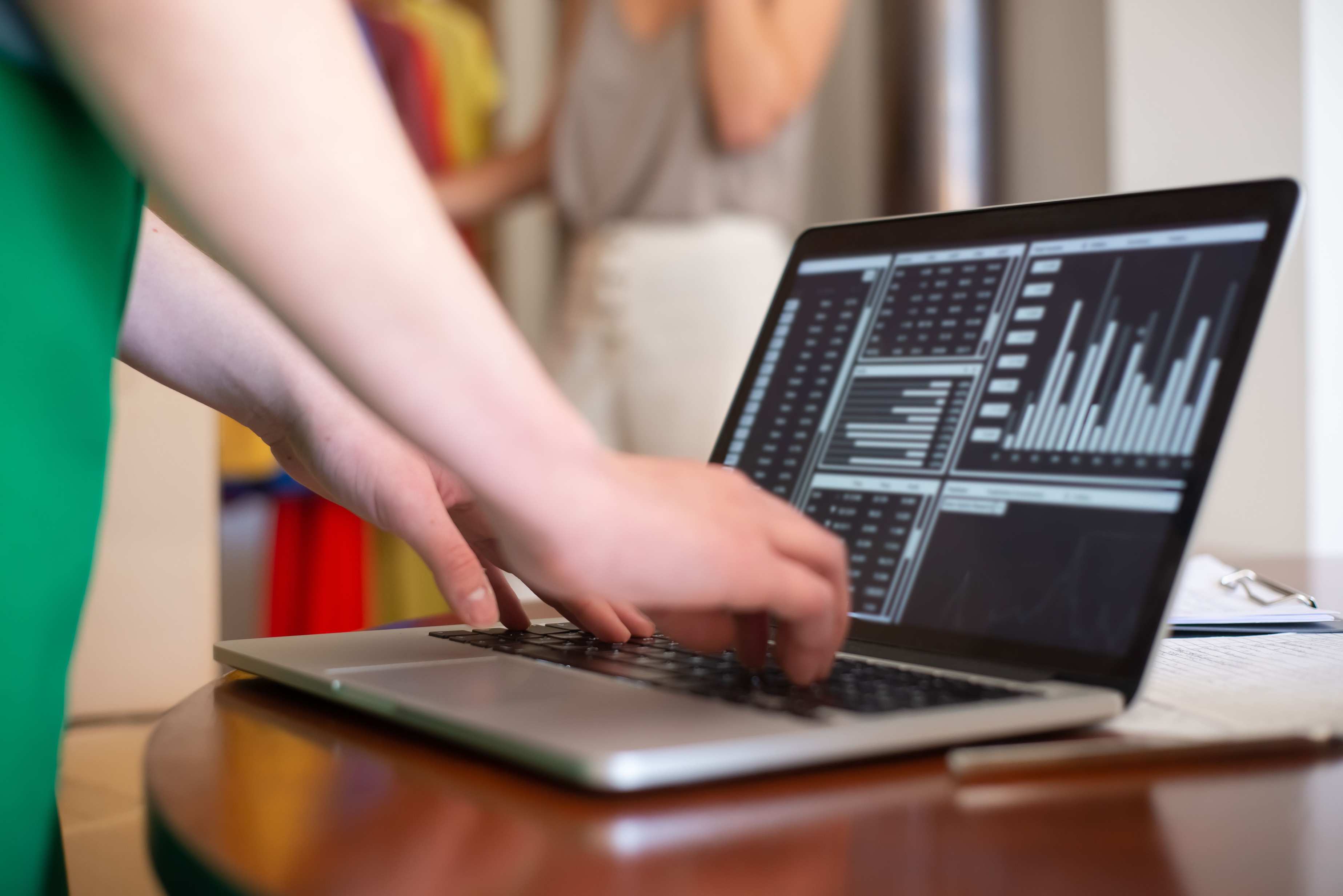 Hände tippen auf einer Laptop-Tastatur; auf dem Bildschirm sind Finanzcharts zu sehen